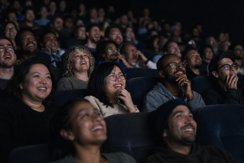 Movie theater audience smiling and reacting together during a shared screening experience.