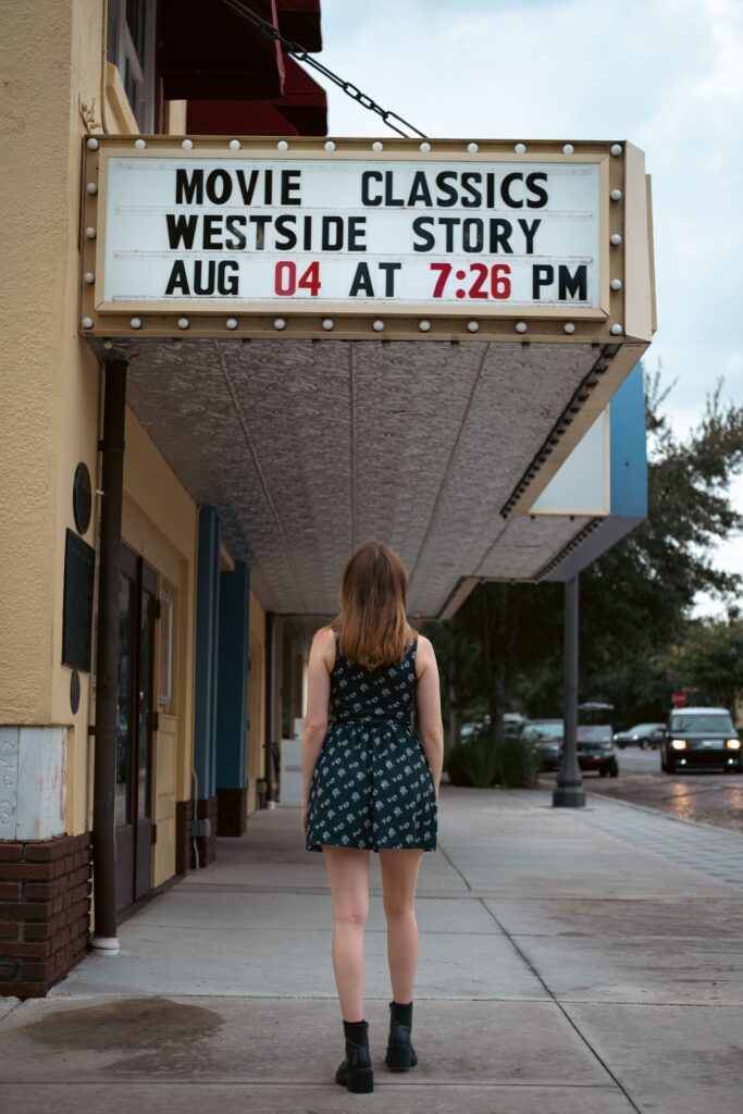 Woman walking toward an independent movie theater marquee advertising a classic screening of West Side Story. Classic programming is a theatrical opportunity